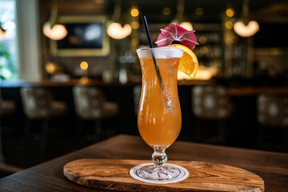 a glass of orange liquid with an umbrella and an umbrella on a wooden surface